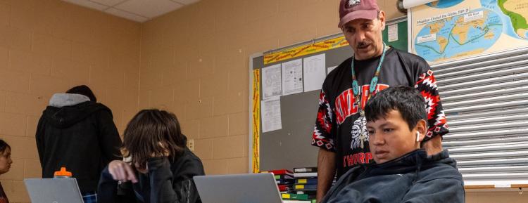 Teacher overlooking students working on laptops in class.