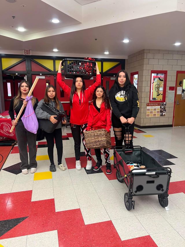 five students in school hallway holding various items