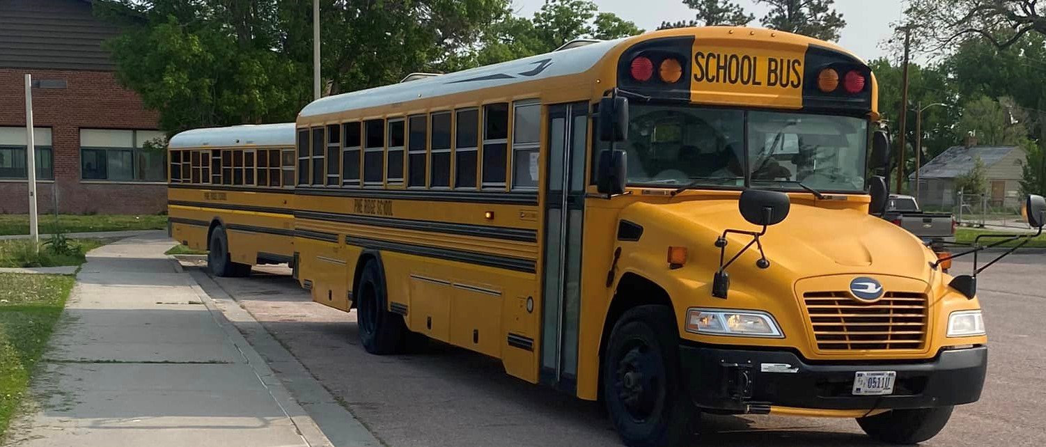 Two school buses parked outside in front of school.